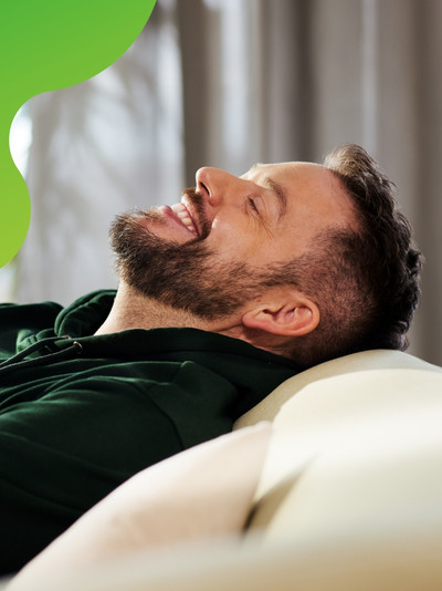 Eine Person lehnt sich auf einem Sofa entspannt zurück und lächelt zufrieden.