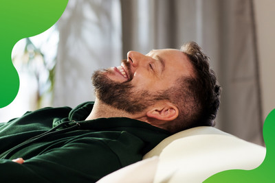 Eine Person lehnt sich auf einem Sofa entspannt zurück und lächelt zufrieden.