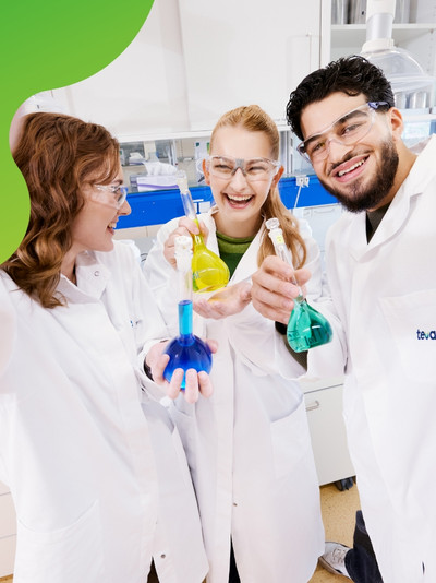 Drei junge Personen in einem Labor die lachen und Reagenzgläser in der Hand halten.