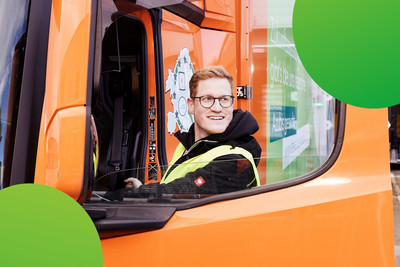 Mann steigt in einen orangen LKW ein und schaut lachend auf die Seite 