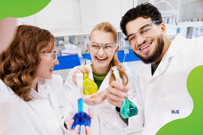 Drei junge Personen in einem Labor die lachen und Reagenzgläser in der Hand halten.