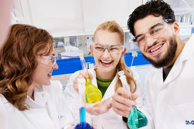 Drei junge Personen in einem Labor die lachen und Reagenzgläser in der Hand halten.