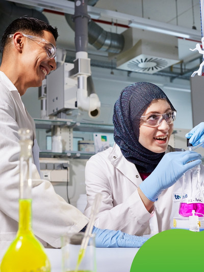 Zwei junge Menschen im Labor hantieren mit bunten Flüssigkeiten und führen einen Versuch durch. 