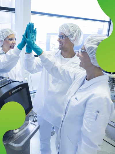 Drei Mitarbeitende im Labor stehen zueinander und geben sich lachend ein High Five. 