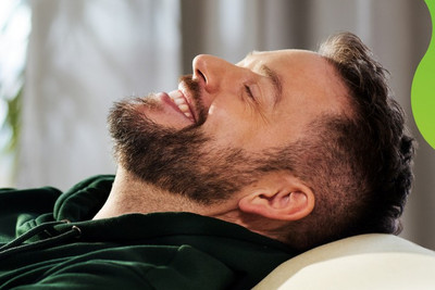 Eine Person lehnt sich auf einem Sofa entspannt zurück und lächelt zufrieden.