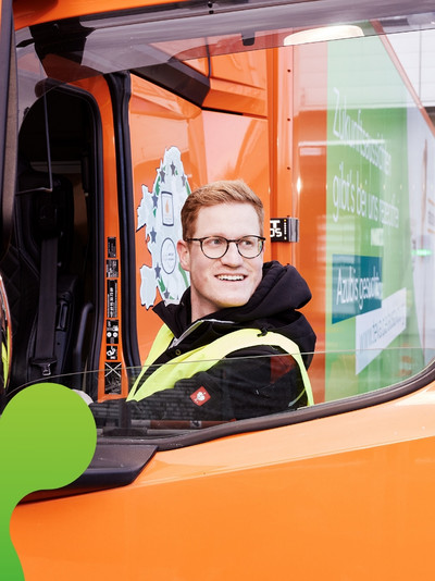 Mann steigt in einen orangen LKW ein und schaut lachend auf die Seite 
