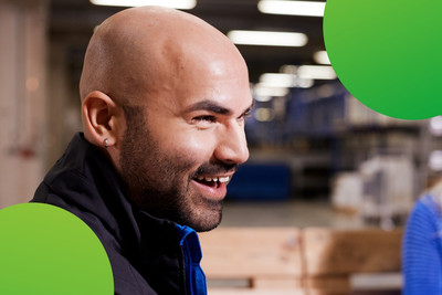 Ein Mann wird von der Seite gezeigt. Er lacht. Im Hintergrund ist eine lachende Frau zu erkennen. 