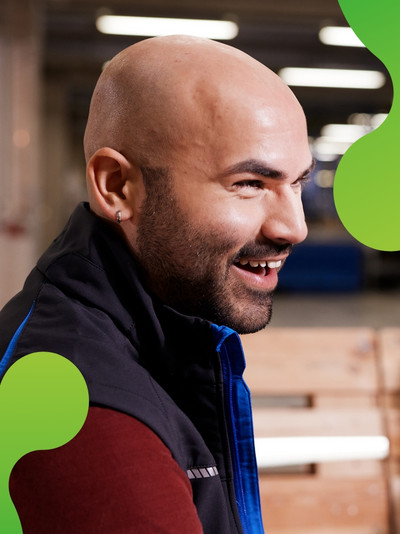 Ein Mann wird von der Seite gezeigt. Er lacht. Im Hintergrund ist eine lachende Frau zu erkennen. 