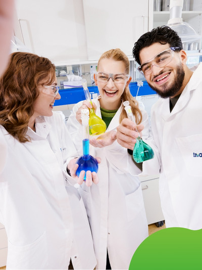 Drei junge Personen in einem Labor die lachen und Reagenzgläser in der Hand halten.