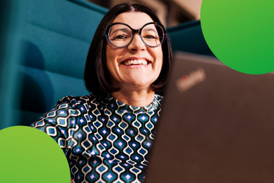 Eine Person schaut lachend in die Kamera. Vor der Person steht ein Laptop.