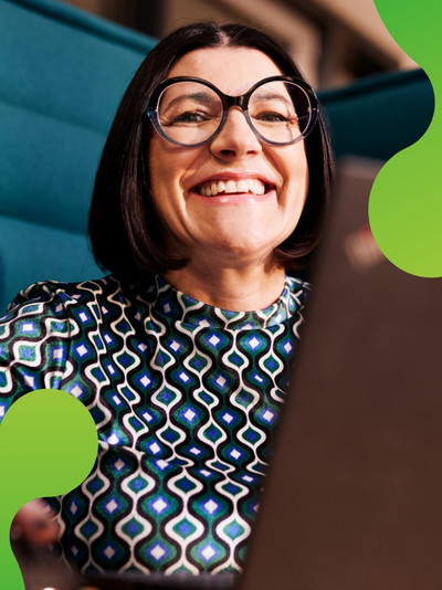 Eine Person schaut lachend in die Kamera. Vor der Person steht ein Laptop.