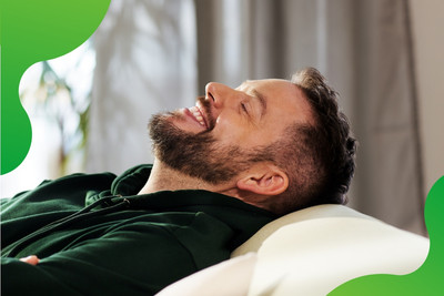 Eine Person lehnt sich auf einem Sofa entspannt zurück und lächelt zufrieden.