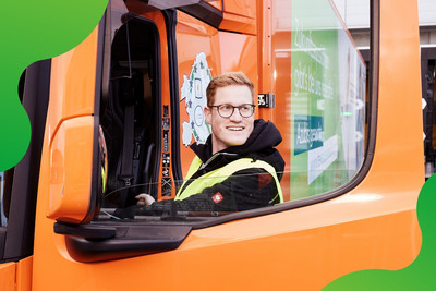 Mann steigt in einen orangen LKW ein und schaut lachend auf die Seite 