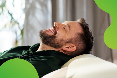 Eine Person lehnt sich auf einem Sofa entspannt zurück und lächelt zufrieden.