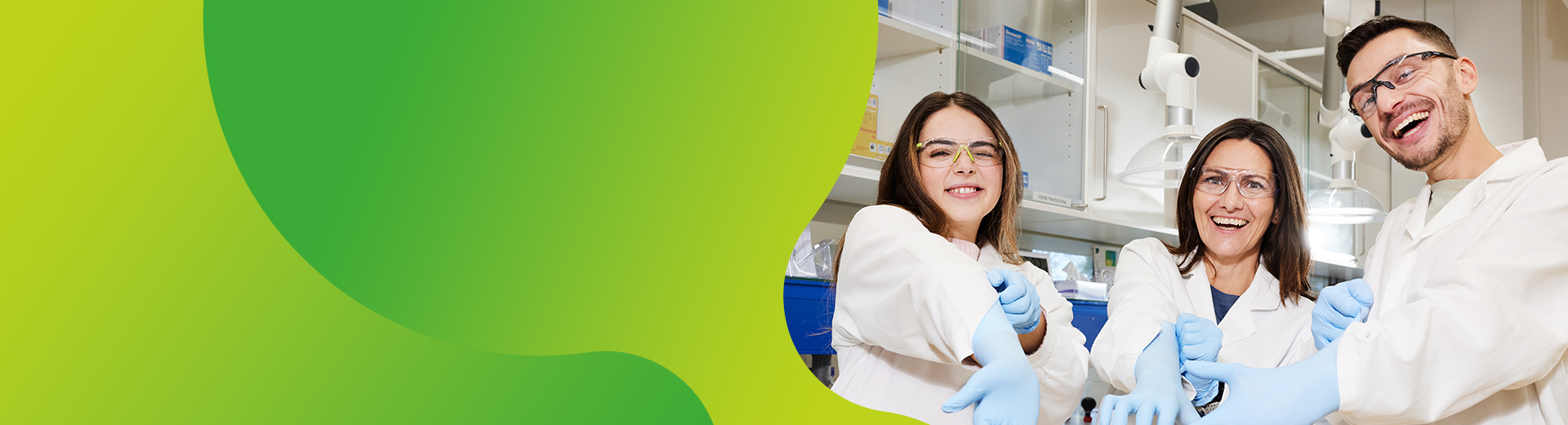 Drei junge Personen in einem Labor die lachen und Reagenzgläser in der Hand halten.