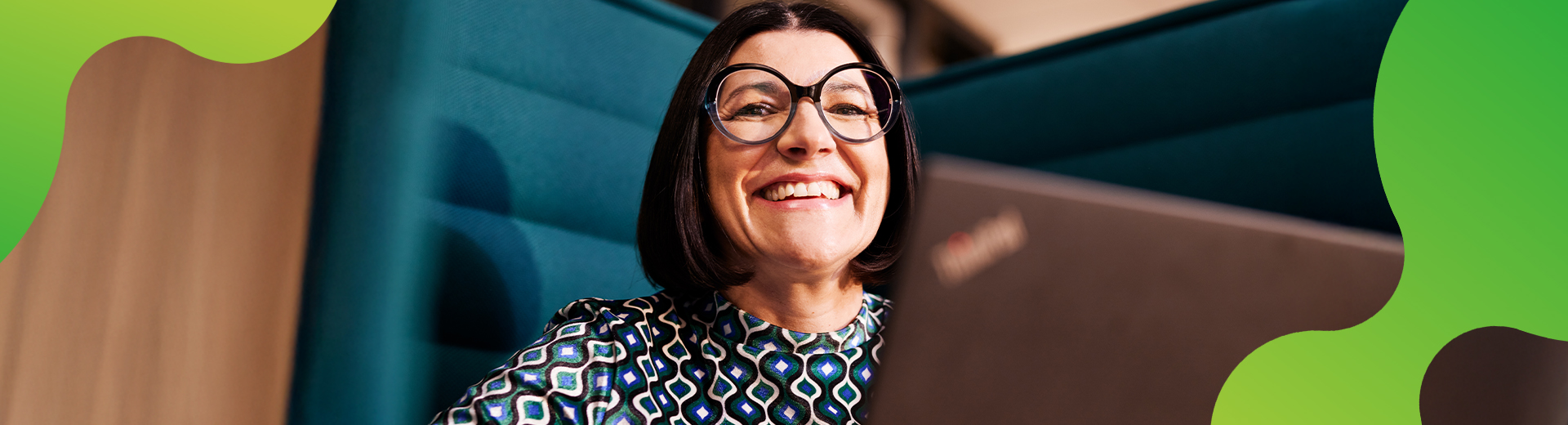 Eine Person schaut lachend in die Kamera. Vor der Person steht ein Laptop.