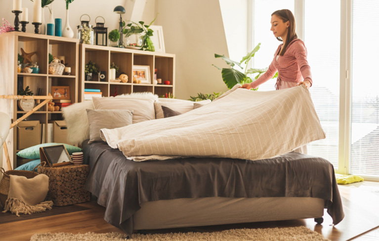 Migräne-betroffene Frau macht ihr Bett mit einer neuen Haushaltsstrategie