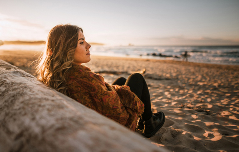 Eine Frau sitzt gedankenverloren am Strand und grübelt darüber, welche Entscheidung für sie als MS-Betroffene die richtige ist – Kinder ja oder nein?