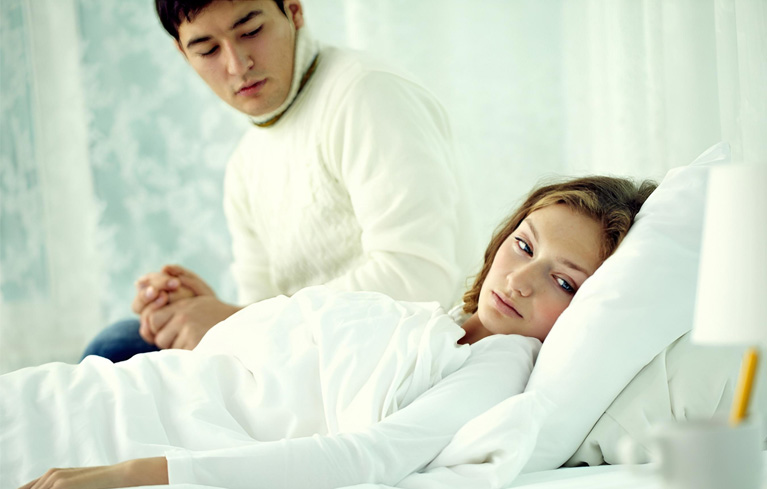 Ein Mann sitzt am Bett seiner kranken Frau und hält ihre Hand