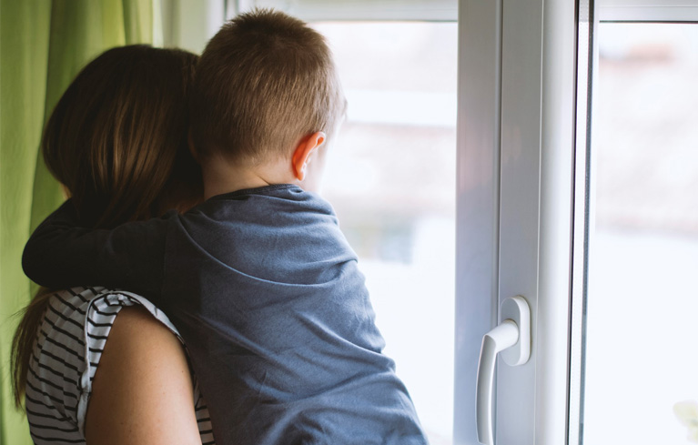 Mutter, die mit dem Sohn aus dem Fenster schaut und über die Zukunft mit MS und ihrer Familie nachdenkt 