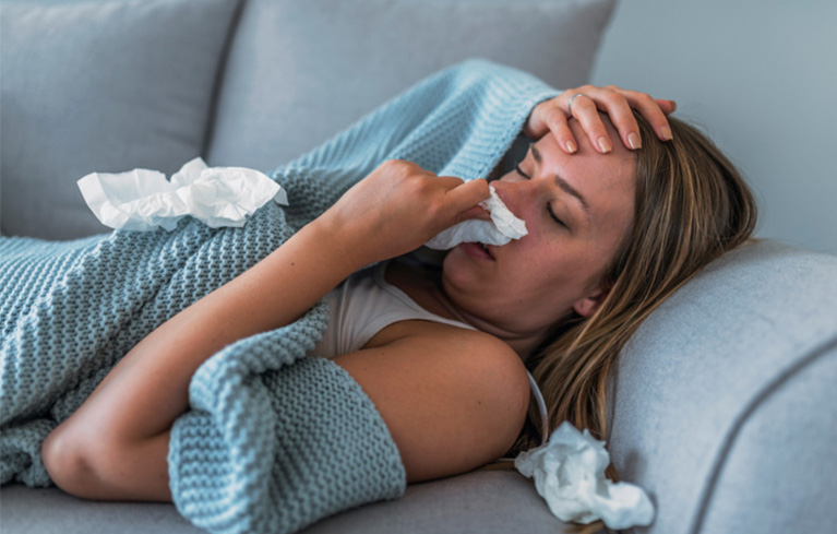 Frau liegt auf dem Sofa und schneuzt sich die Nase