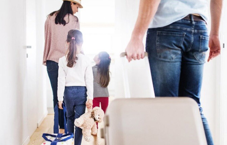 Eine Familie mit 2 kleinen Mädchen geht mit Gepäck zur Wohnungstür, um in den Urlaub zu starten