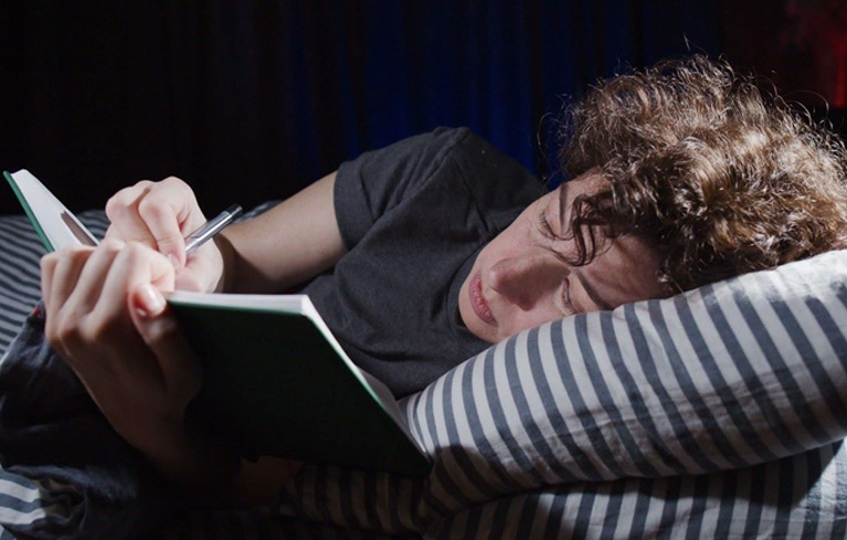 Frau, die ihre Sorgen über das Imposter-Syndrom und die chronische Erkrankung im Bett liegend in einem Tagebuch notiert.