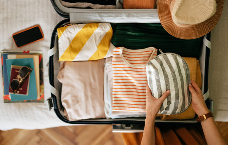 Frau packt die wichtigsten Dinge für einen Urlaub mit Migräne ein, einschließlich Sonnenbrille und Hut