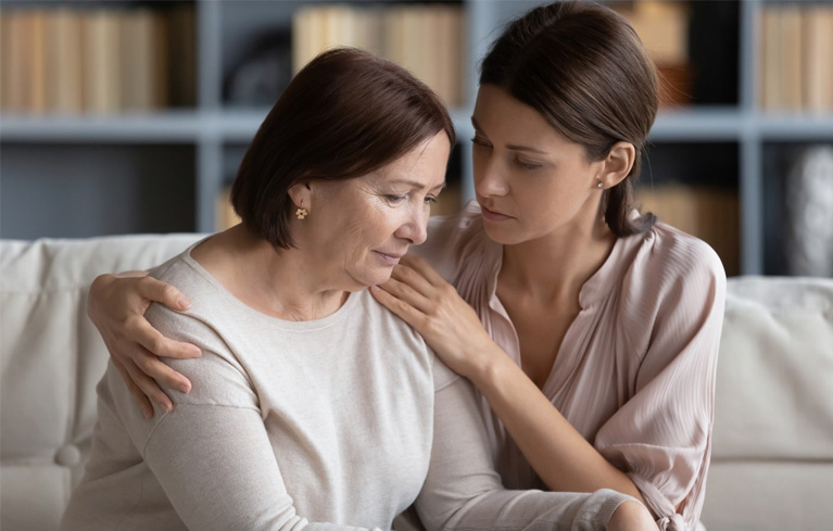 Eine Tochter sitzt mit ihrer dementen Mutter auf dem Sofa und umarmt sie.