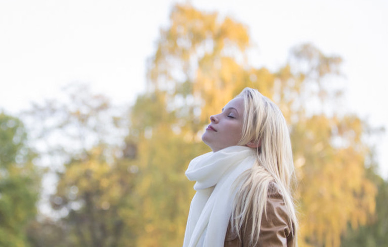 Eine Frau steht mit geschlossenen Augen in der Natur und genießt die frische Luft.