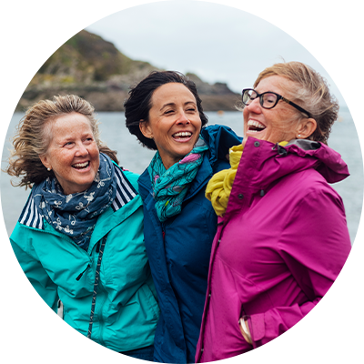 Drei Frauen stehen in bunten Regenjacken lachend beieinander